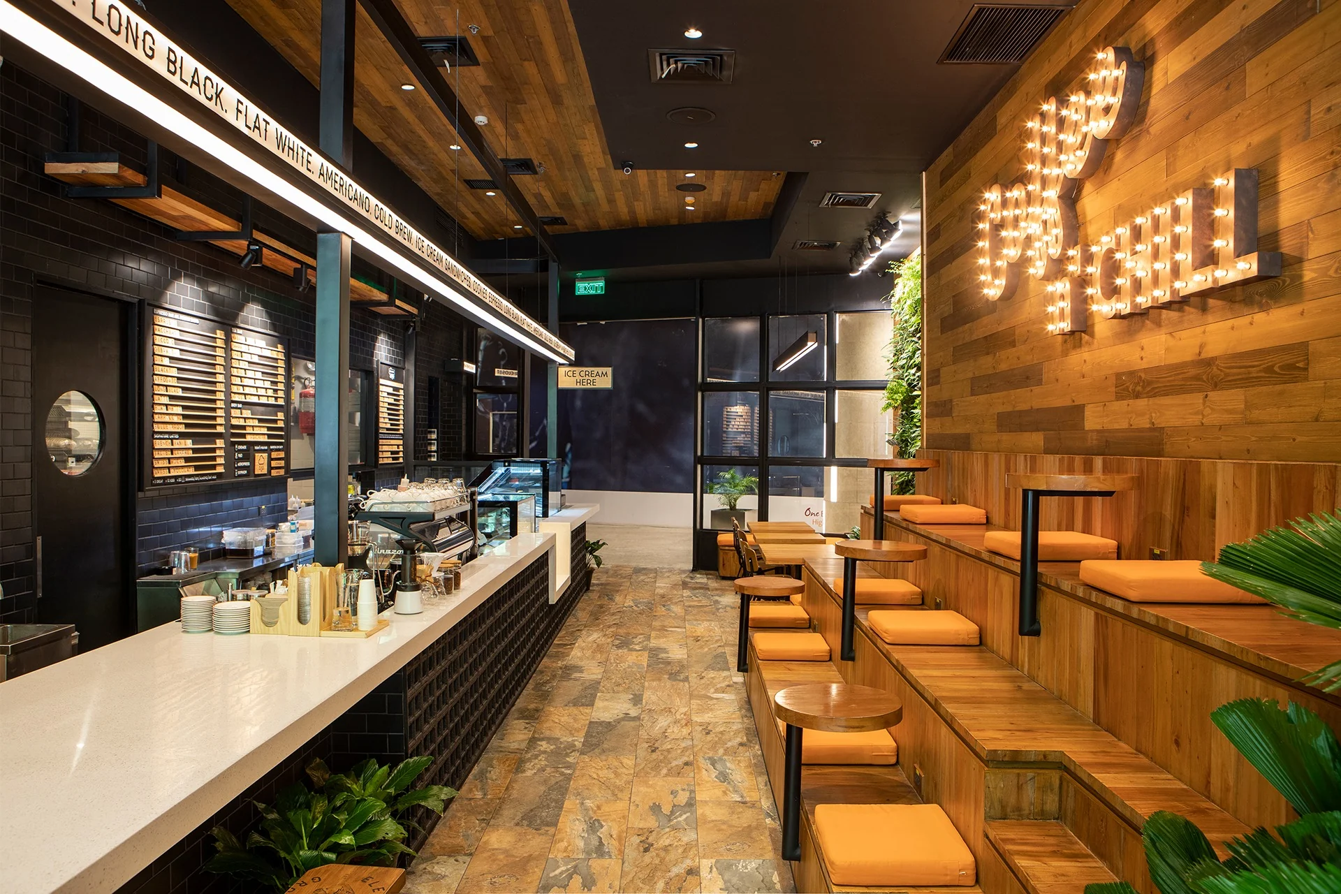 Warm wood-lined café interior with a long coffee counter, seating, and illuminated wall lettering.